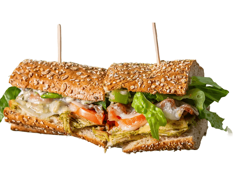 A vibrant chicken and cheese sandwich on a seeded baguette with lettuce, pesto, and sun-dried tomatoes, served on a white plate.