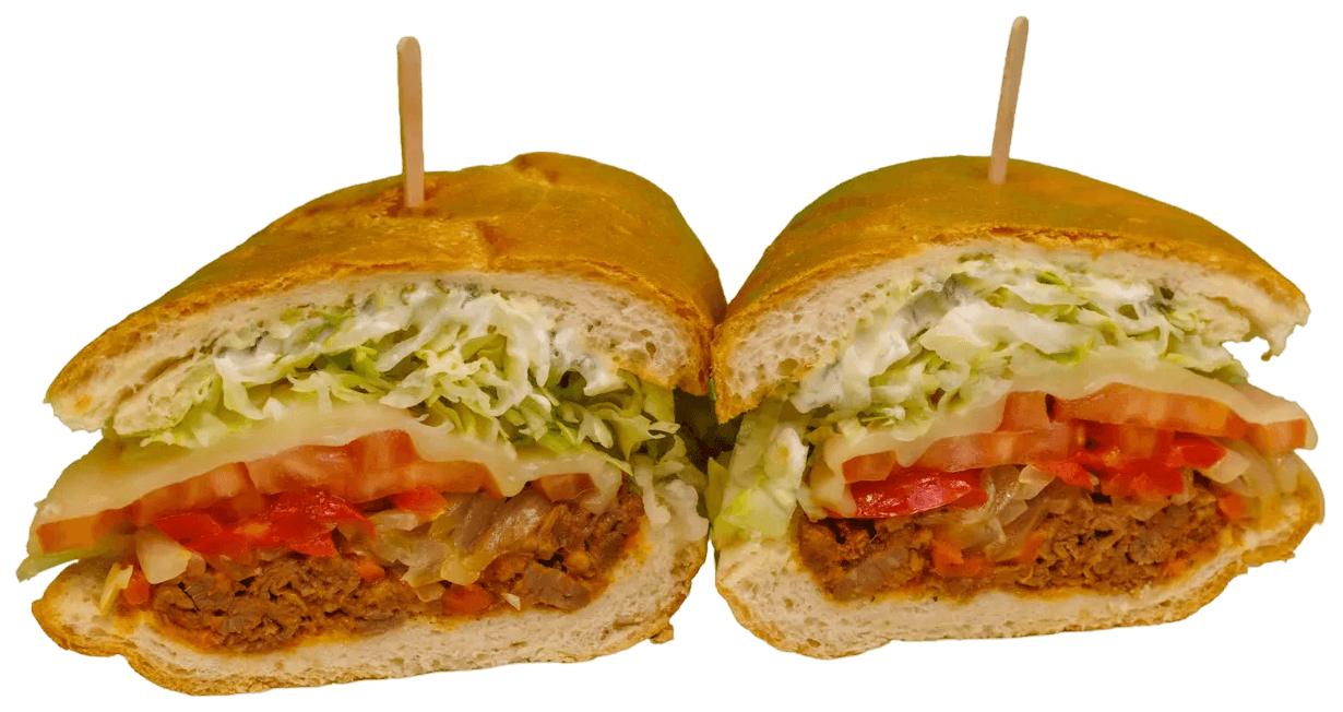 A large golden-brown sub sandwich, sliced in half, revealing layers of savory shredded meat, sautéed onions and peppers, melted cheese, tomatoes, shredded lettuce, and a creamy white sauce. Two toothpicks are visible.