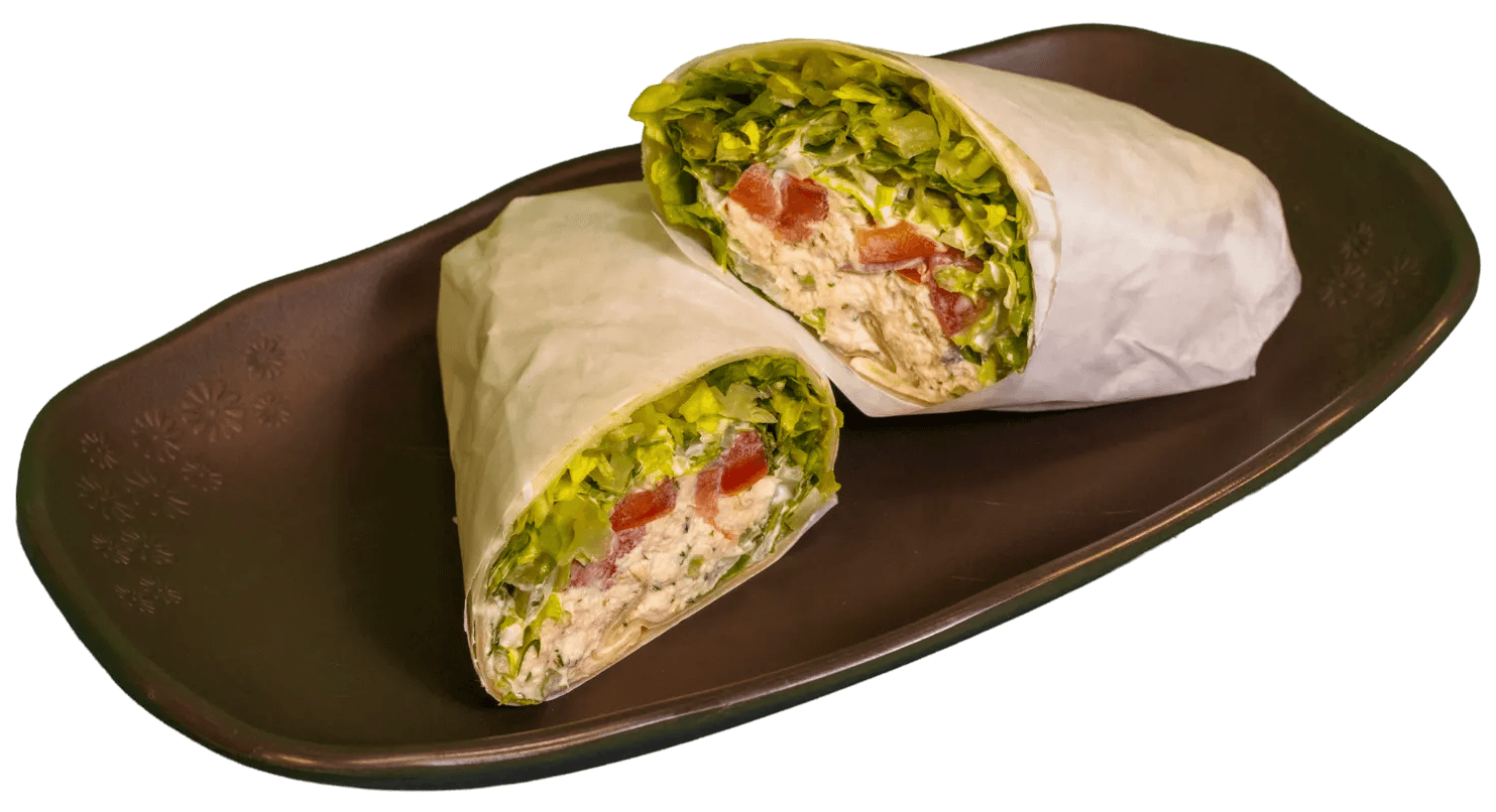 Two wraps, cut in half, display fillings of white meat, red cabbage, carrots, a creamy sauce, fresh green herbs, and red spice.