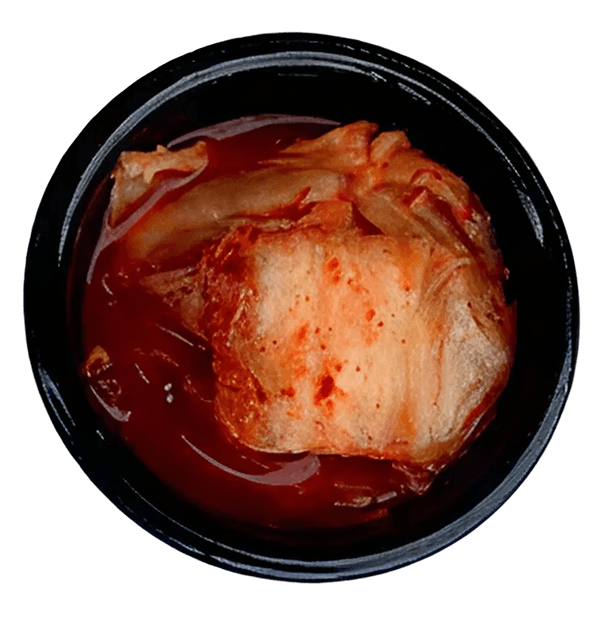 Top-down view of a black bowl filled with reddish-orange kimchi in a dark red sauce.
